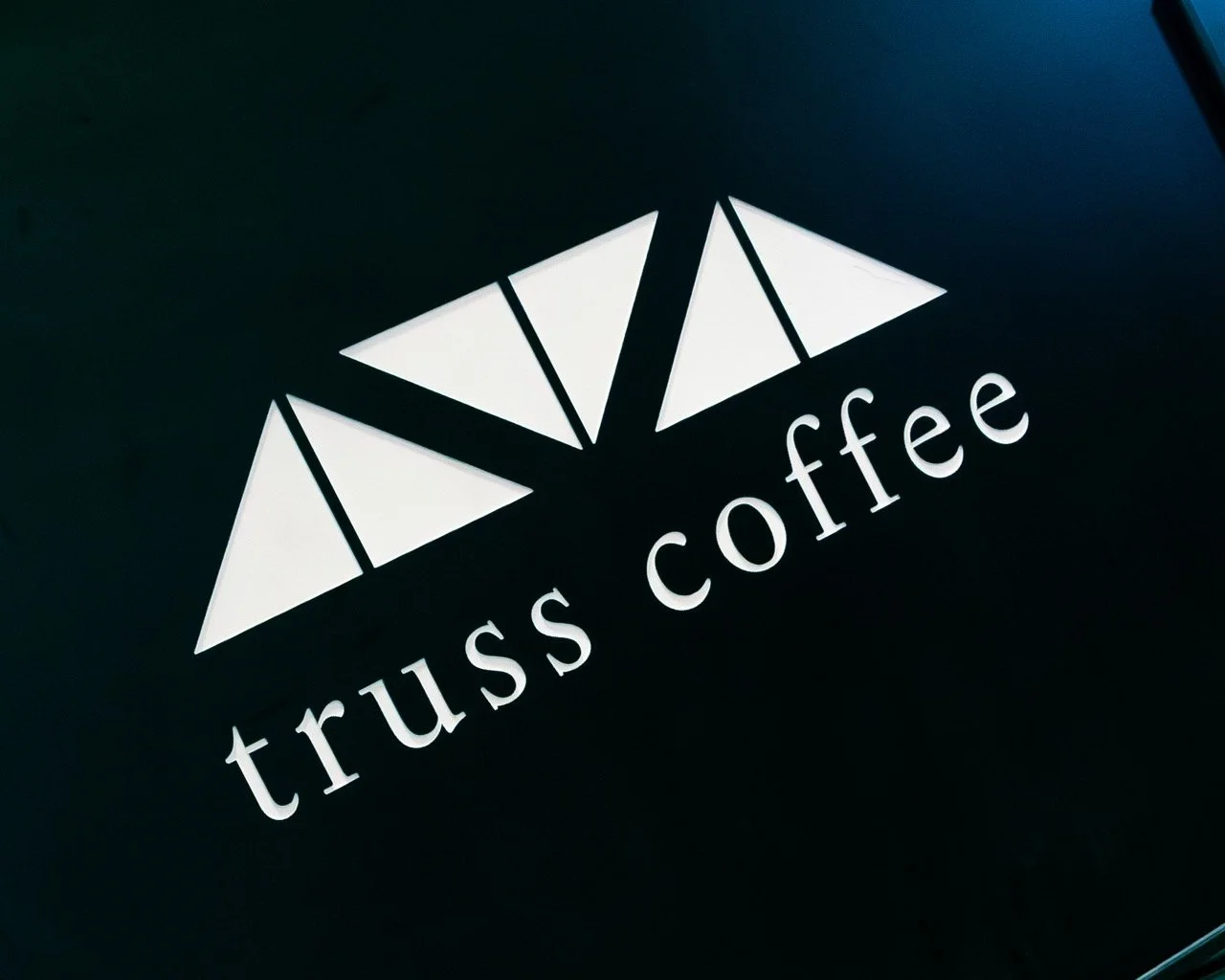 Logo and brand photography of, "truss coffee" local to the DC area in NOMA. White Truss Coffee logo on a black background