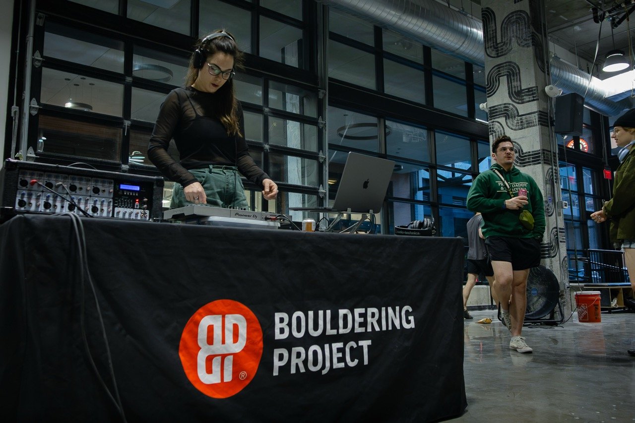Bouldering Project table as DJ, Jess Gioe plays. People nearby drinking beer at a local event