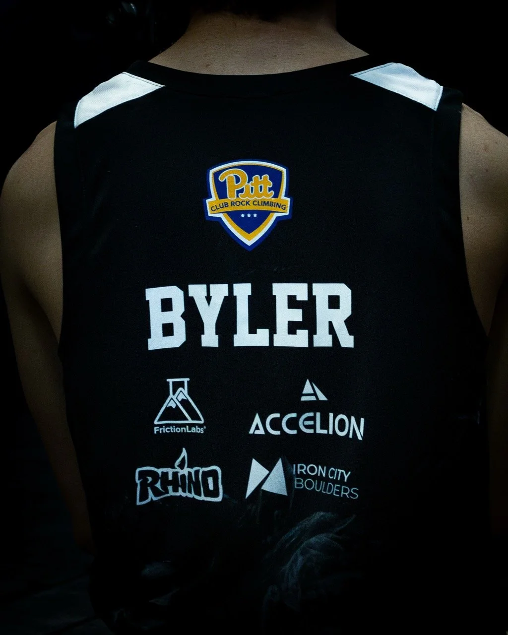 Taken bear DC, The brand of Pitt University Climbing Club's jersey modeled by Byler. Shows other prominent brands such as Friction Labs, Accelion, Rhino, and Iron City Boulders.