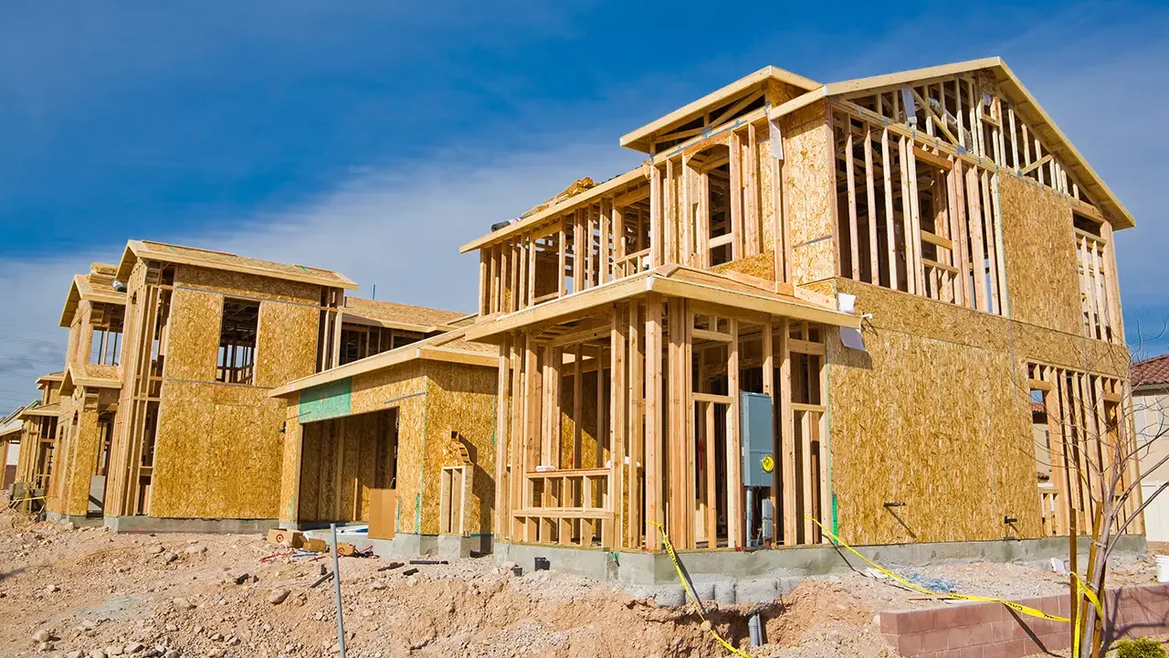 Multiple houses under construction with wooden framing against a blue sky.