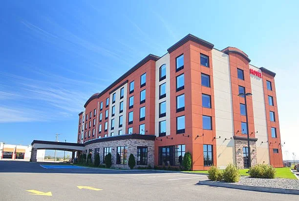 Mid-rise hotel building with a red and beige exterior, multiple windows, and a parking lot in front.