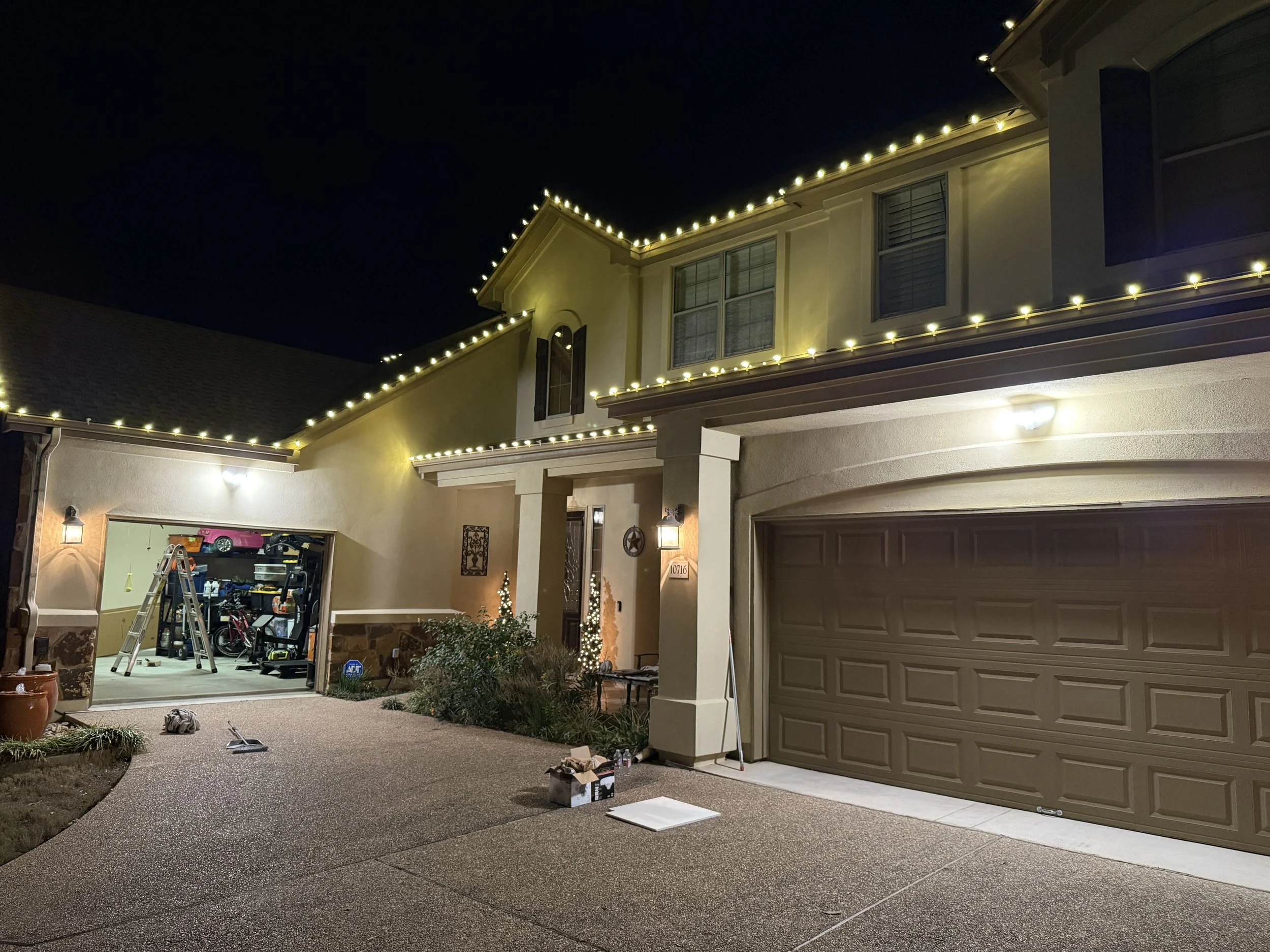 Night view of a house with exterior lighting, two garage doors, and a driveway. floodlights installed both side of garage