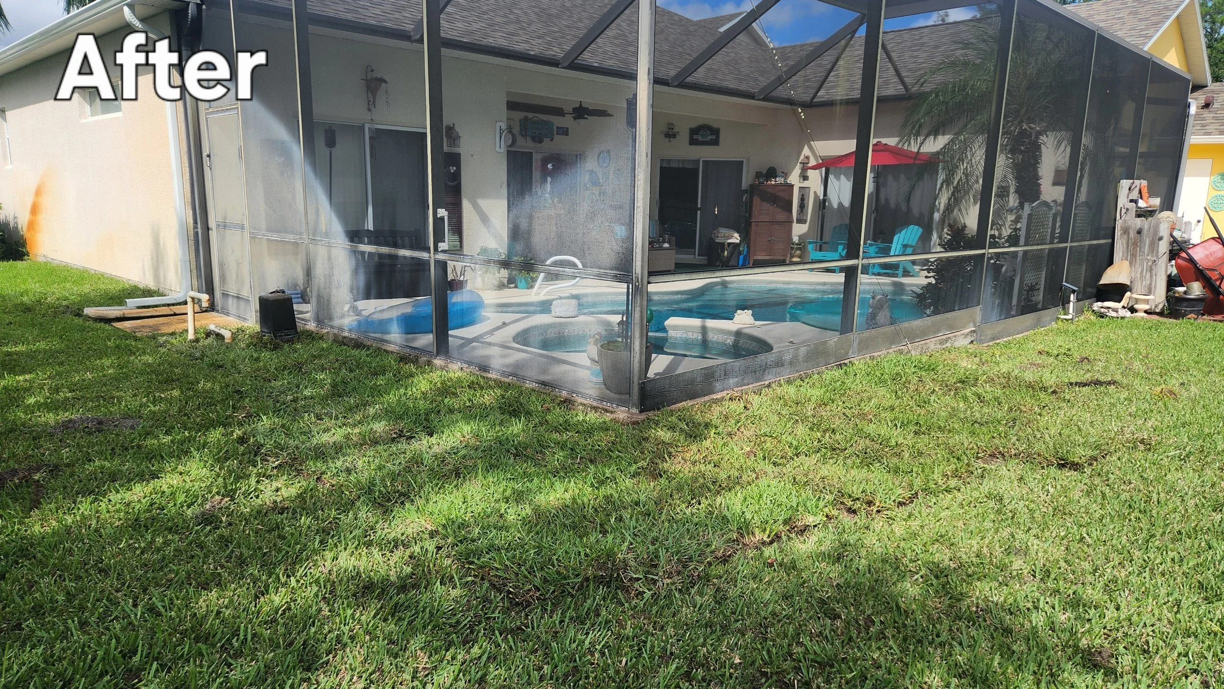 Backyard with screened-in pool area, outdoor furniture, and a red umbrella, surrounded by grass and neighboring houses.