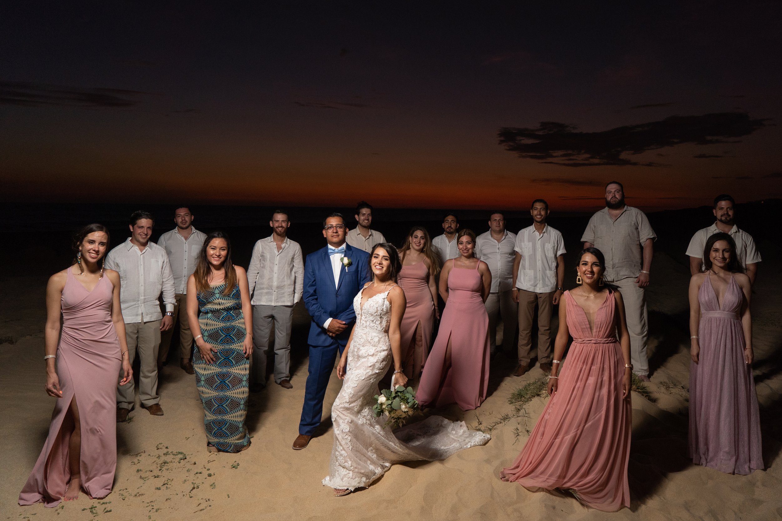 Grupo de personas en una playa durante la puesta de sol, vestidas con ropa formal para una boda.