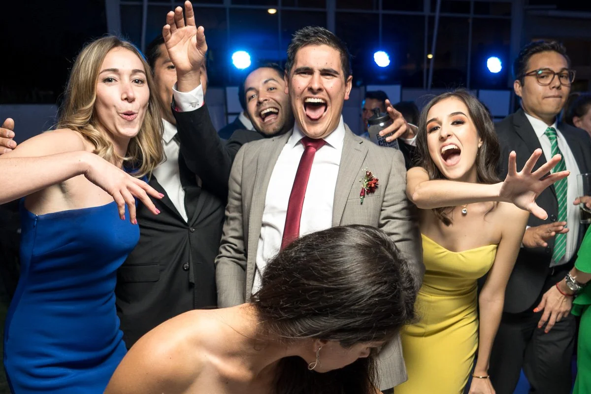 Group of people celebrating and smiling at an indoor party or event, with some raising hands and gesturing.