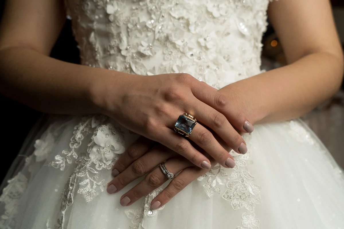 Close-up of a bride's hands with rings, on her wedding dress with floral embroidery.