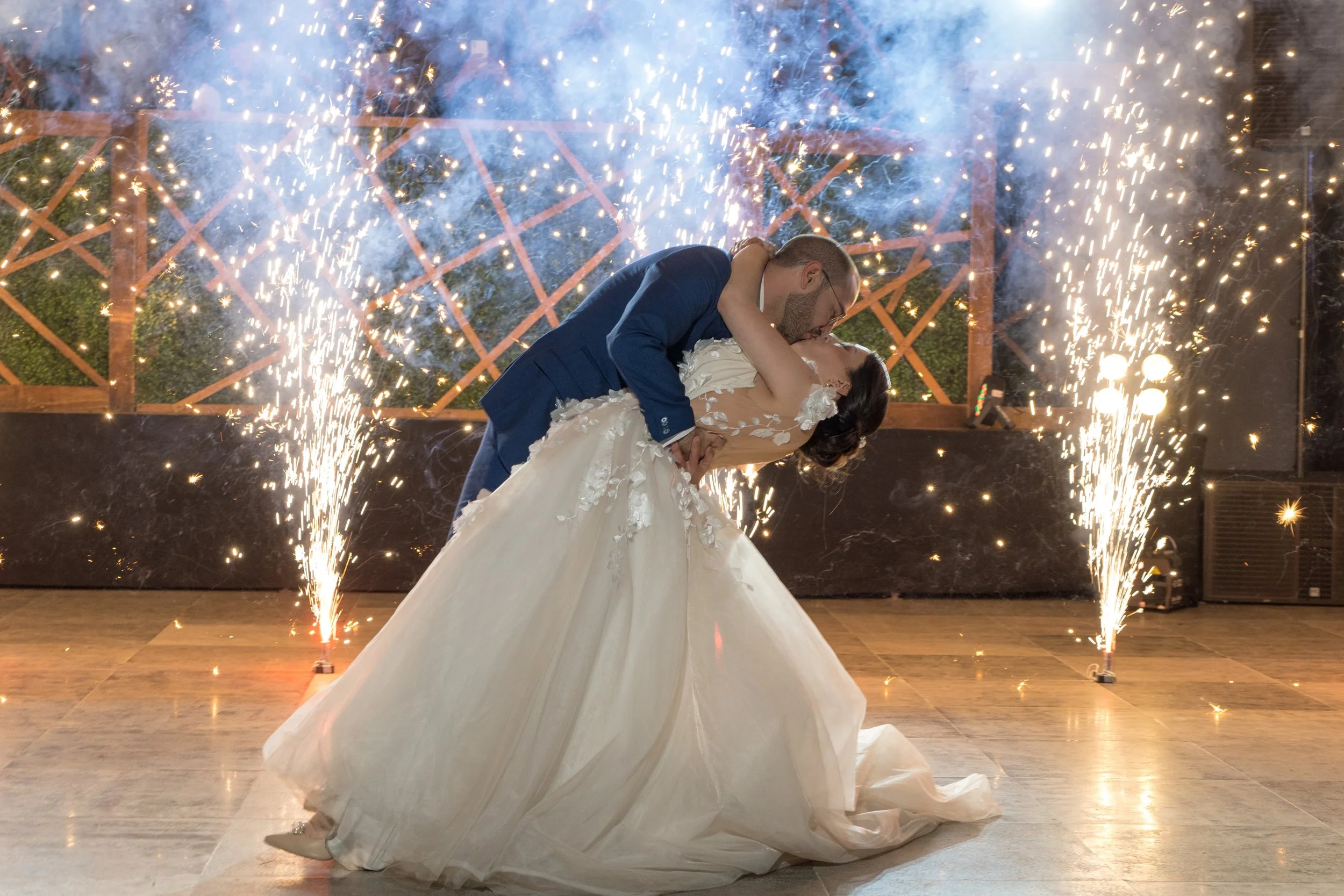una pareja de recién casados en un baile, rodeados de fuegos artificiales y confeti, durante una celebración en interiores