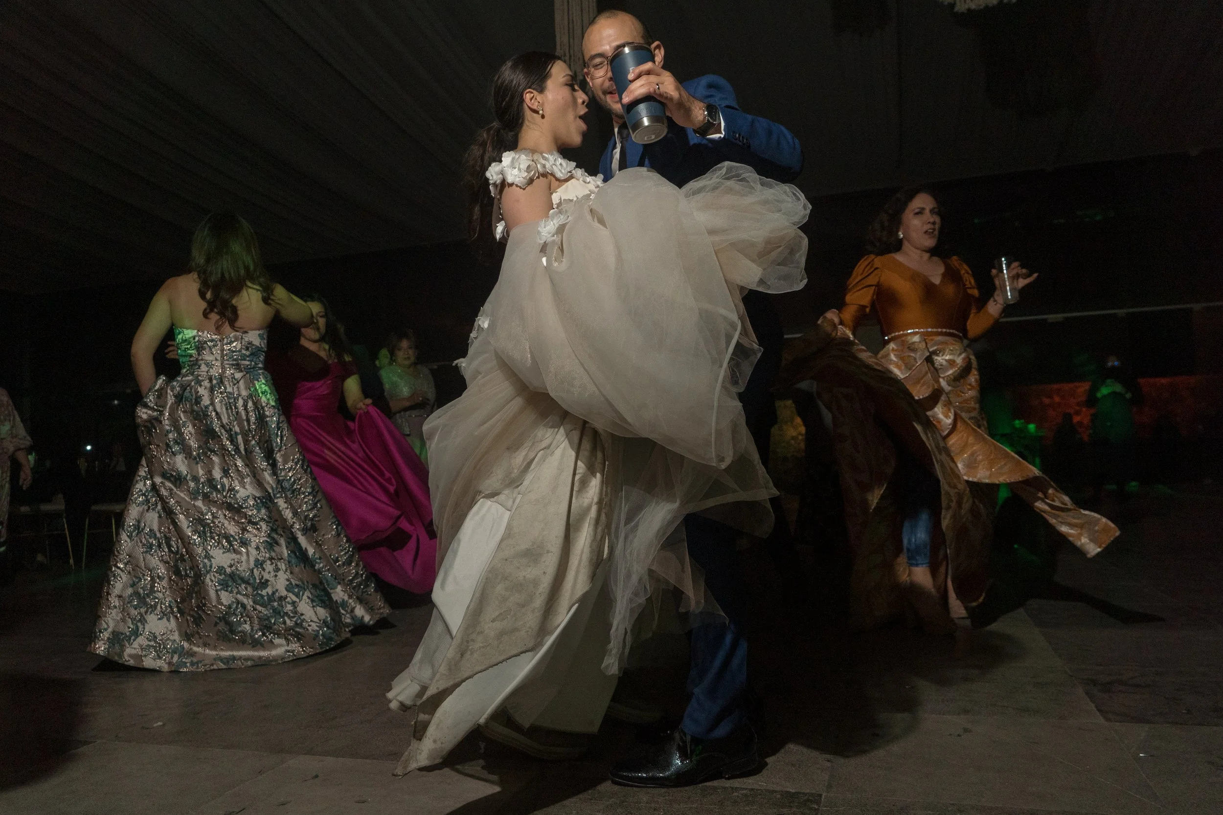 Personas bailando en una fiesta, con vestidos formales y un ambiente oscuro.