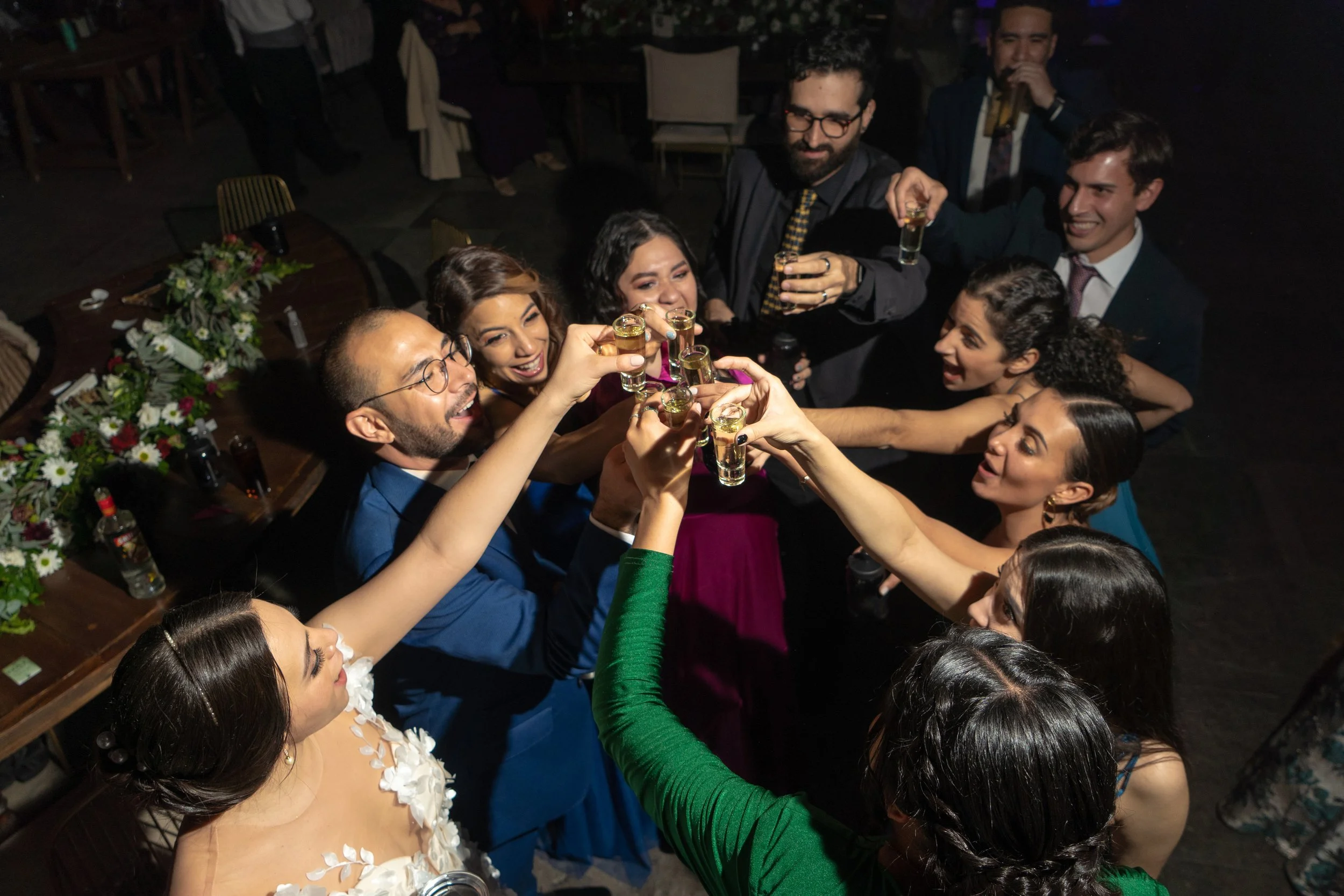 Grupo de personas brindando con pequeños vasos en una celebración o fiesta, en un ambiente festivo y alegre.