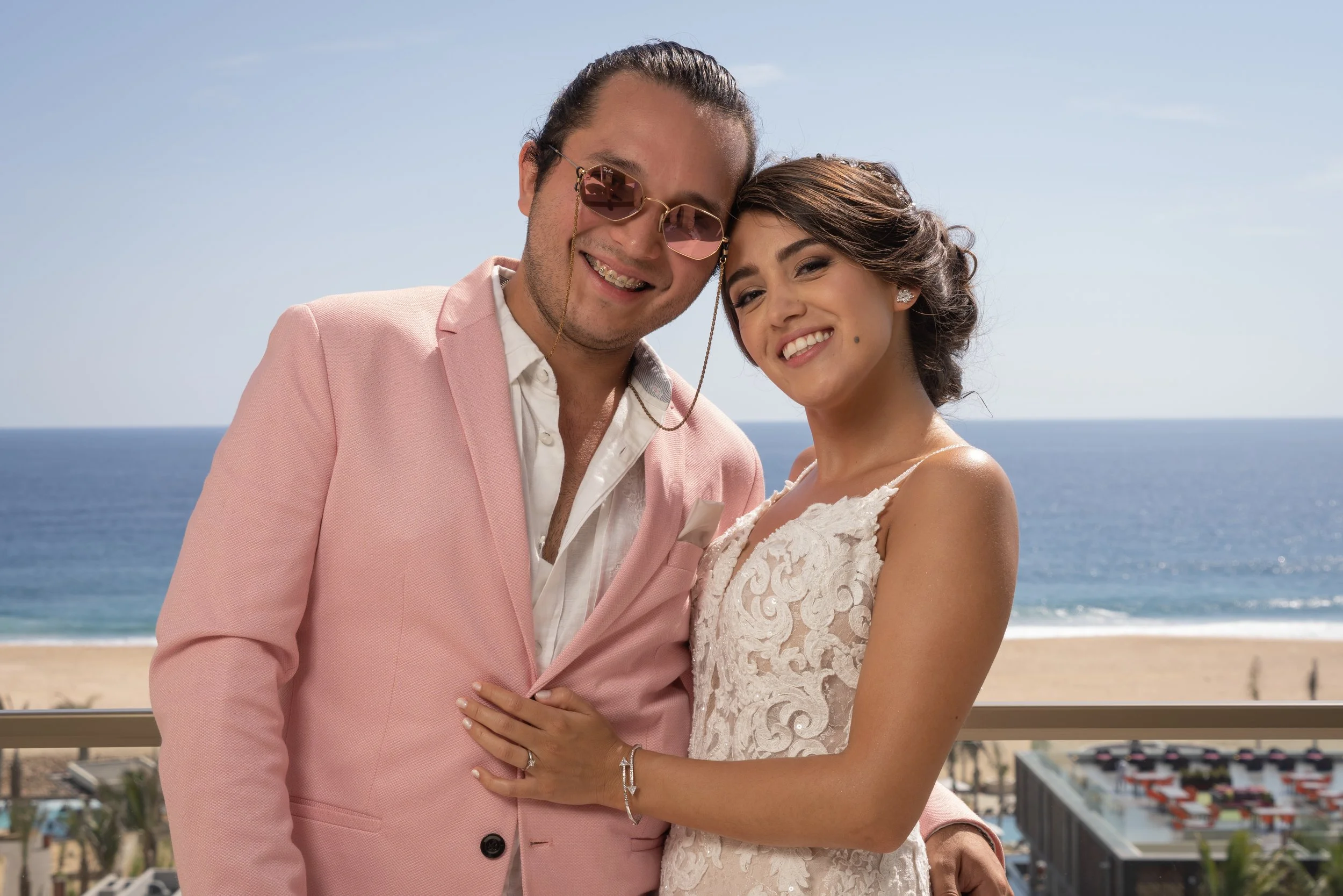 Pareja joven sonriendo en una playa, con el mar y el cielo de fondo.