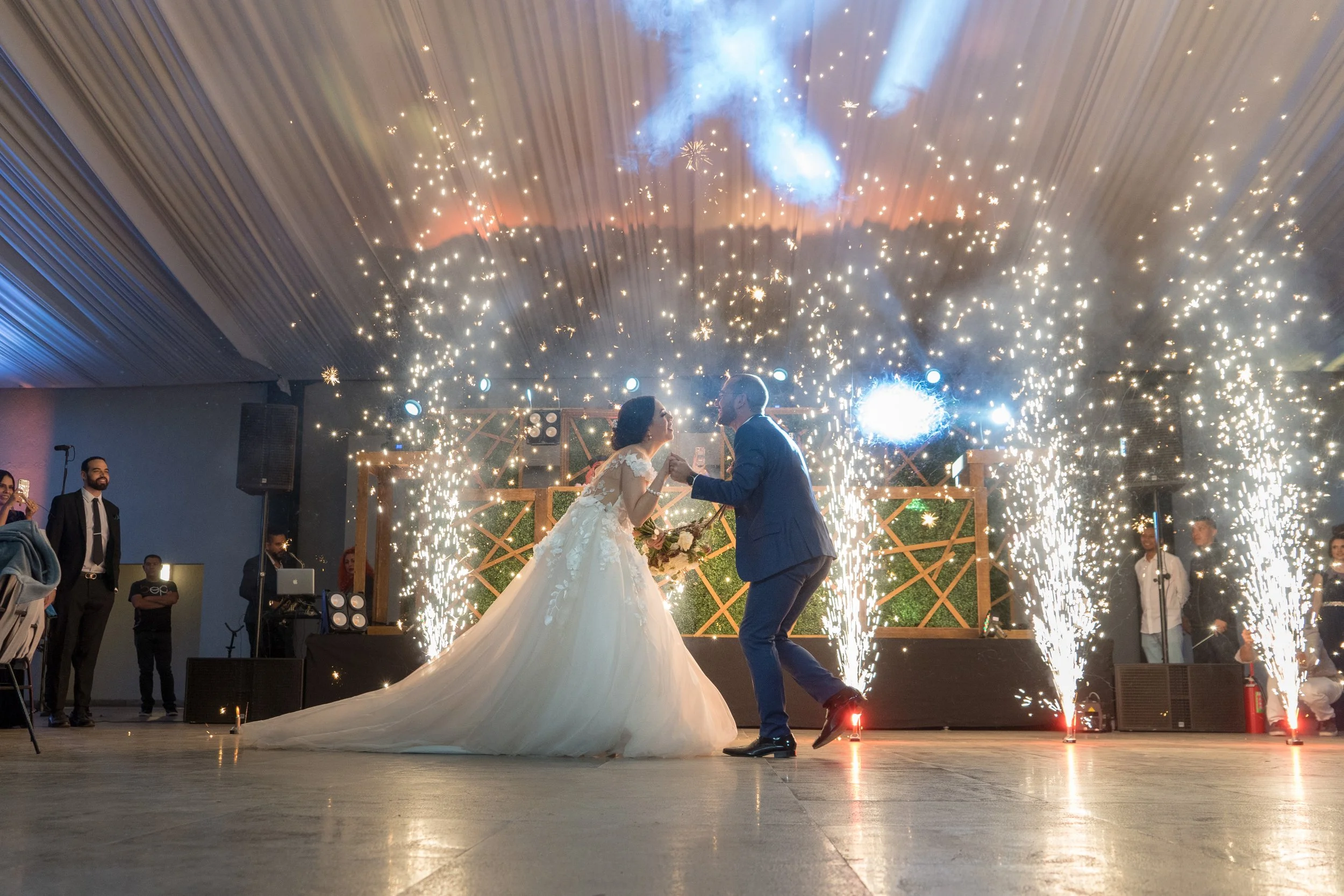 Pareja de novios bailando rodeados de fuegos artificiales en una celebración de boda.