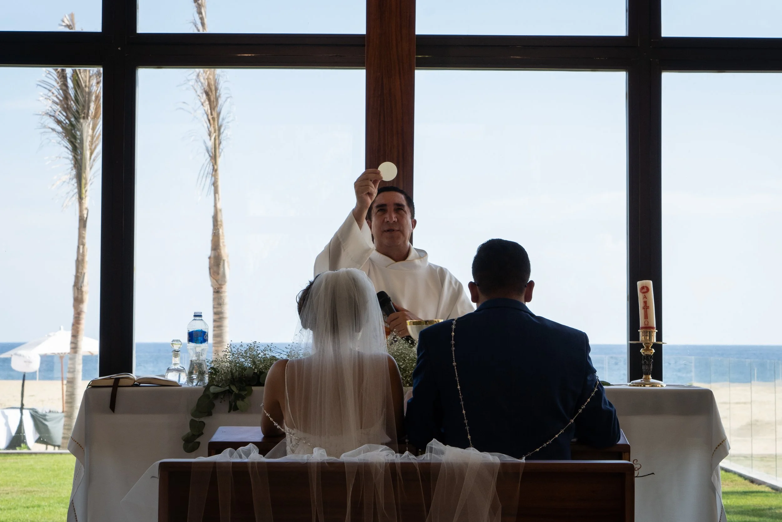 Pareja en boda en una iglesia con vista al mar, con un oficiante en el altar