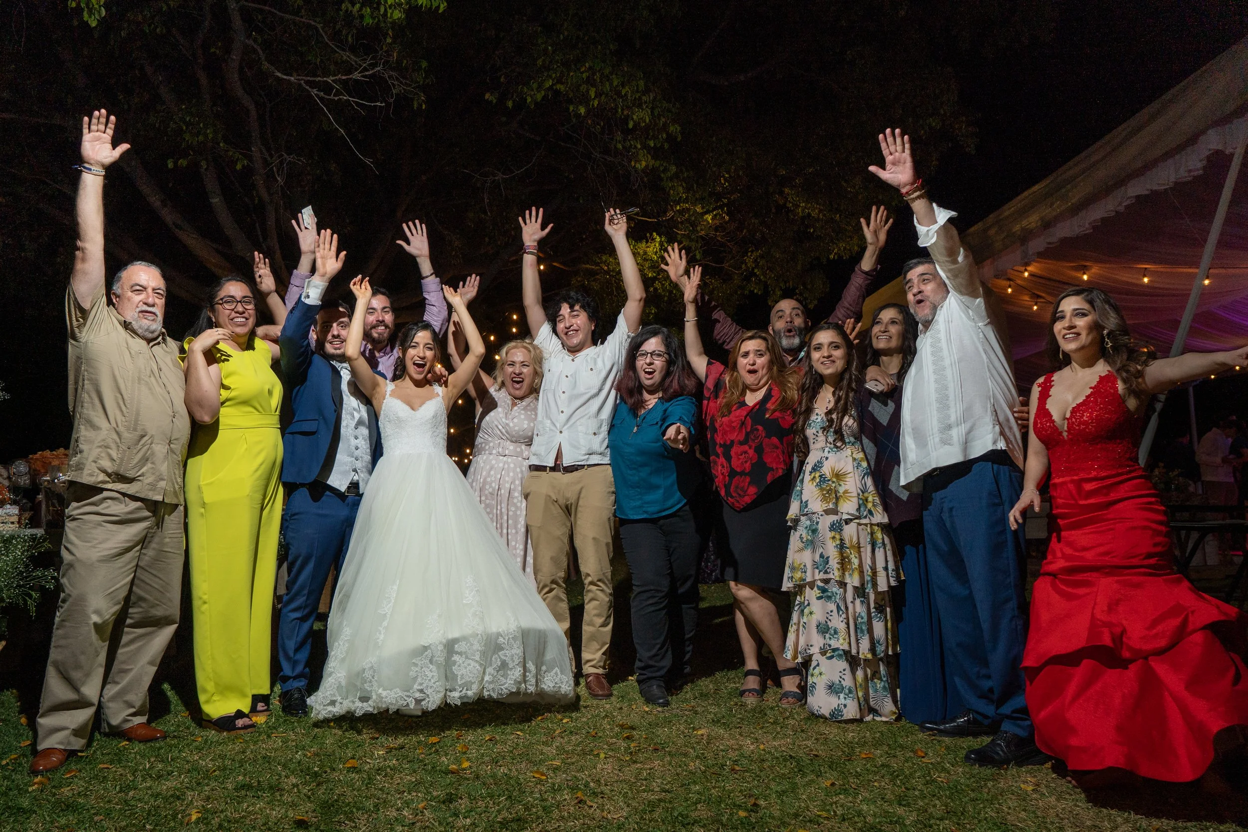 Grupo de personas celebrando en una fiesta al aire libre por una boda, algunos con brazos levantados y sonriendo.