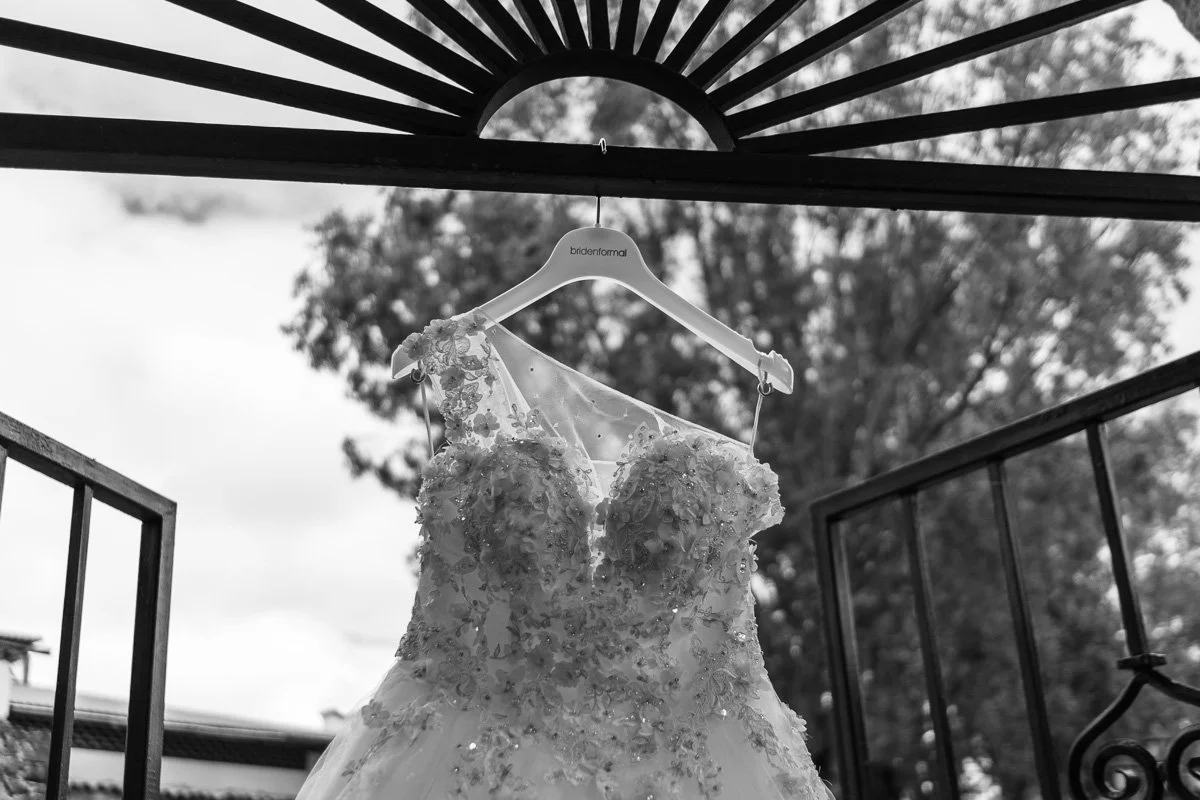 A wedding dress hanging on a hanger outside, with a tree and sky in the background.
