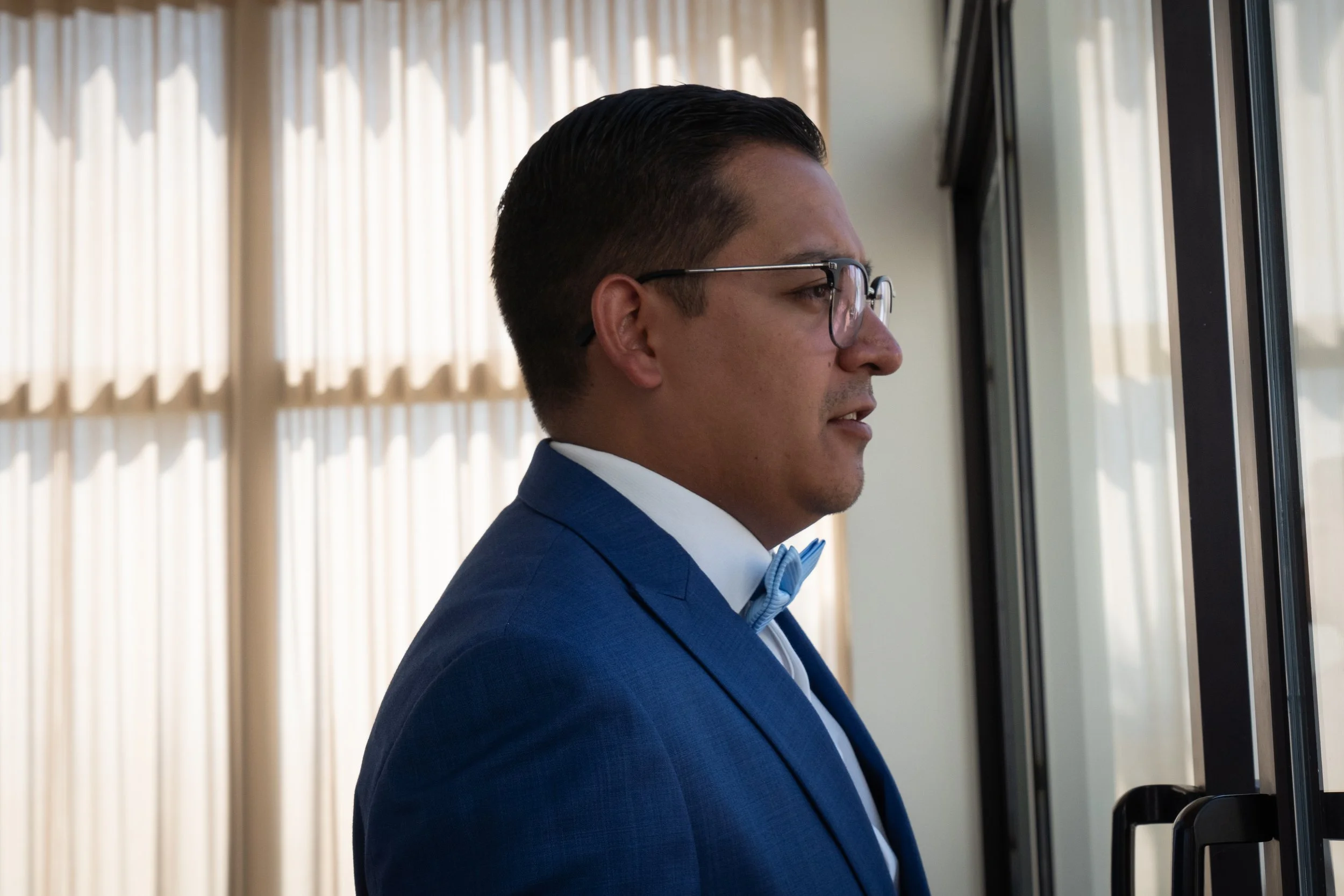 Hombre con gafas y traje azul mirando por la ventana
