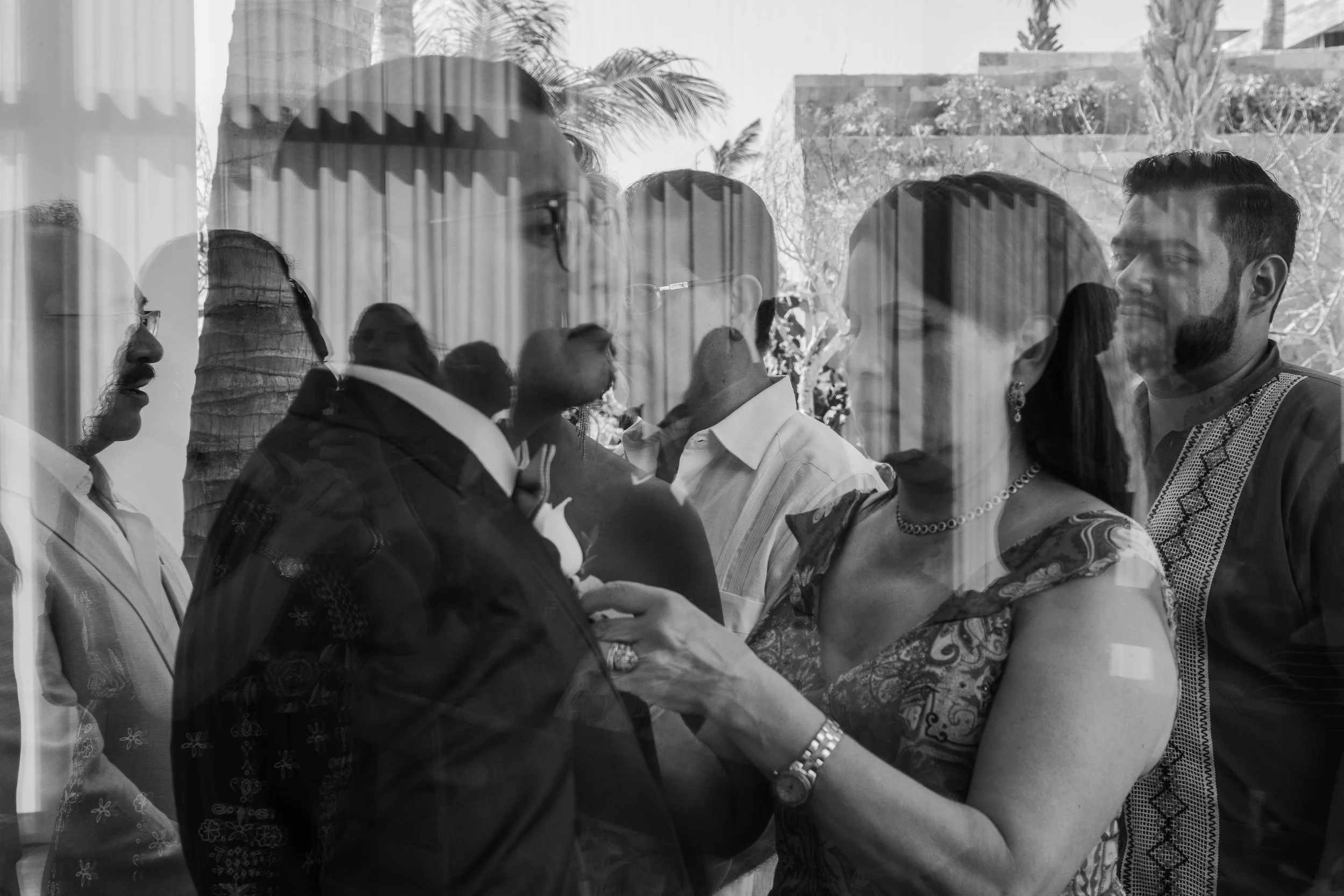 Grupo de personas en una reunión o evento social, visto a través de un ventanal o cristal con reflejos.