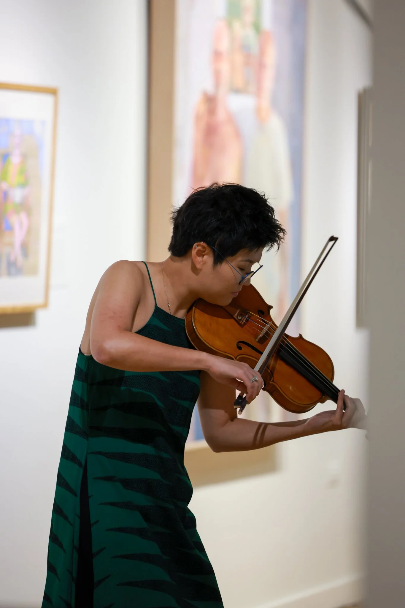 Person wearing a green and black striped dress playing the violin at an art gallery.