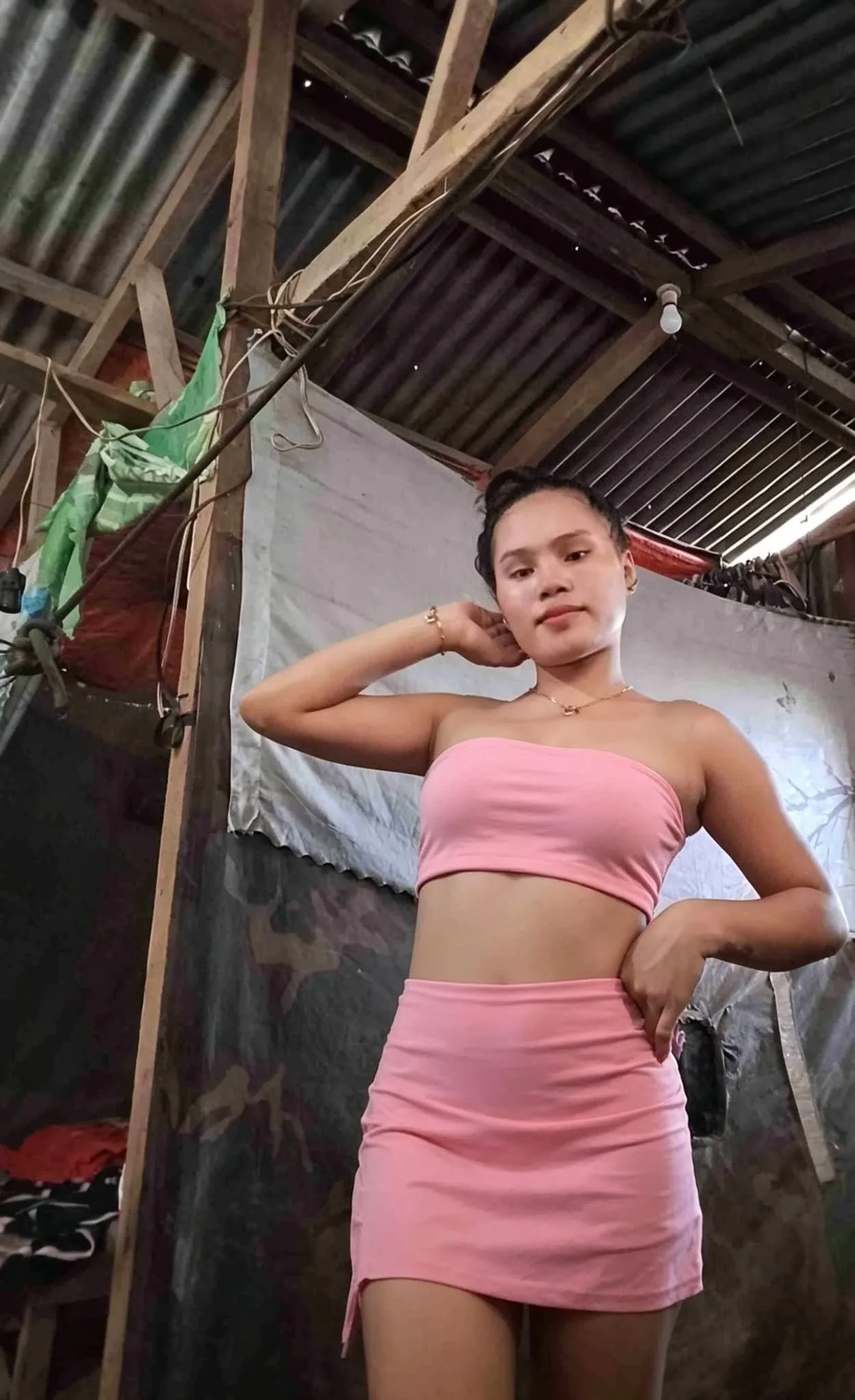 Young woman in pink workout outfit standing indoors with a hand behind her head and a confident expression.
