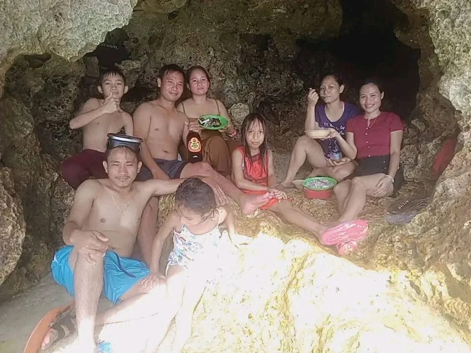 Group of people sitting inside a rocky cave, some with food and drinks, enjoying a casual moment together.