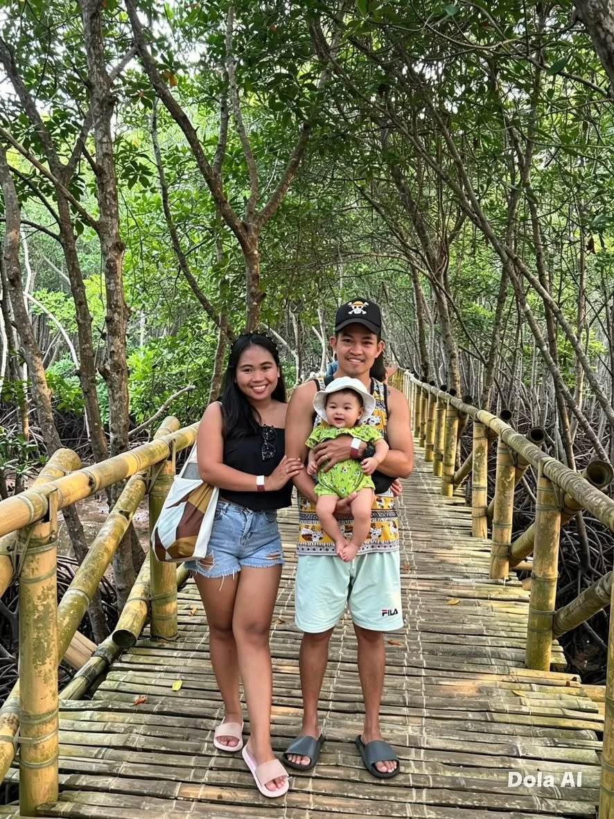 Three people, a man, a woman, and a baby, standing on a wooden bridge in a lush green forest.