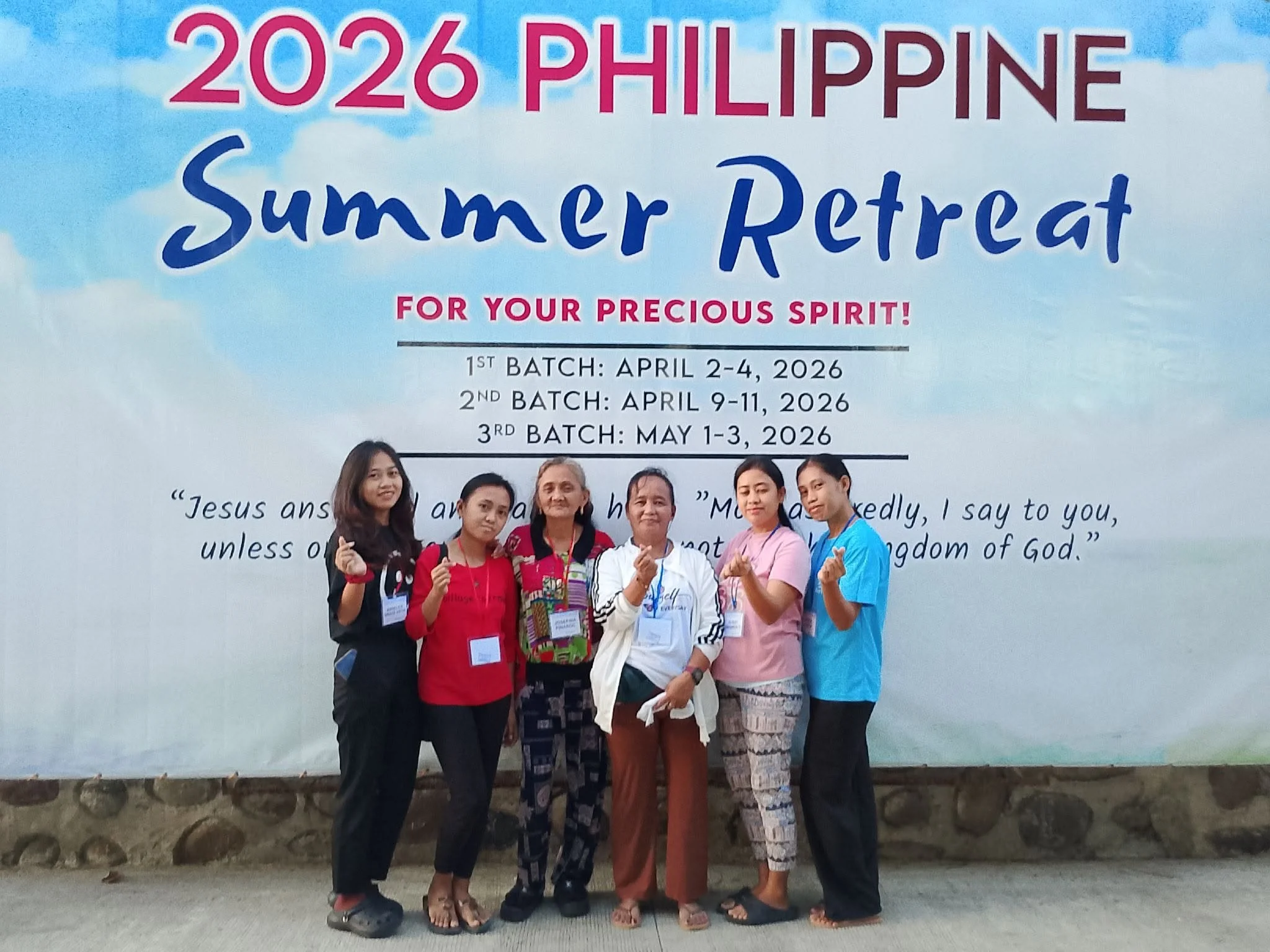 Group of six women standing together in front of a large sign promoting the 2026 Philippine Summer Retreat. The women are smiling, making heart hand gestures, and wearing conference badges.