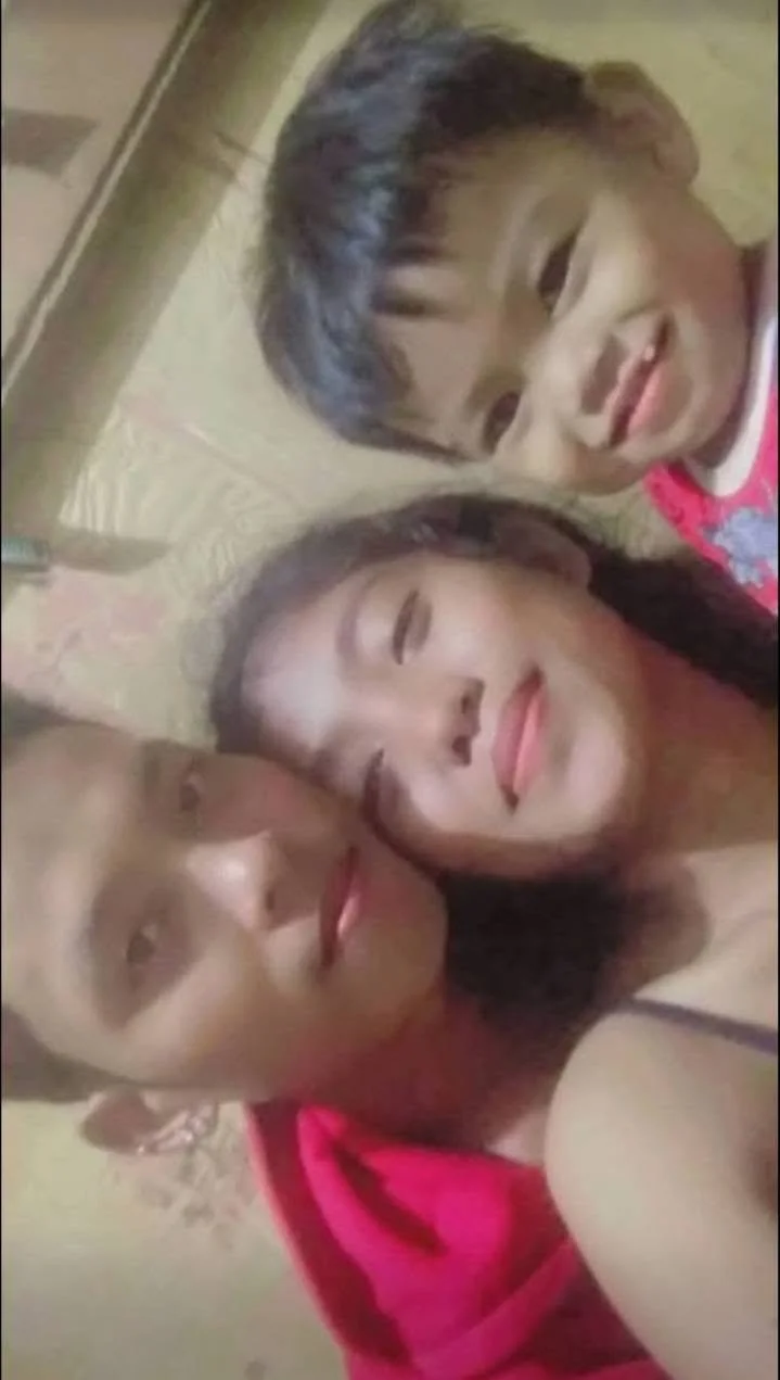 Three children lying on a bed, smiling and taking a selfie.