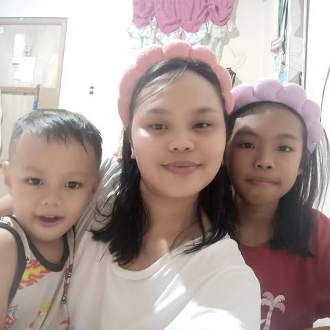 A woman with two young girls, all wearing flower crowns, posing indoors for a selfie.