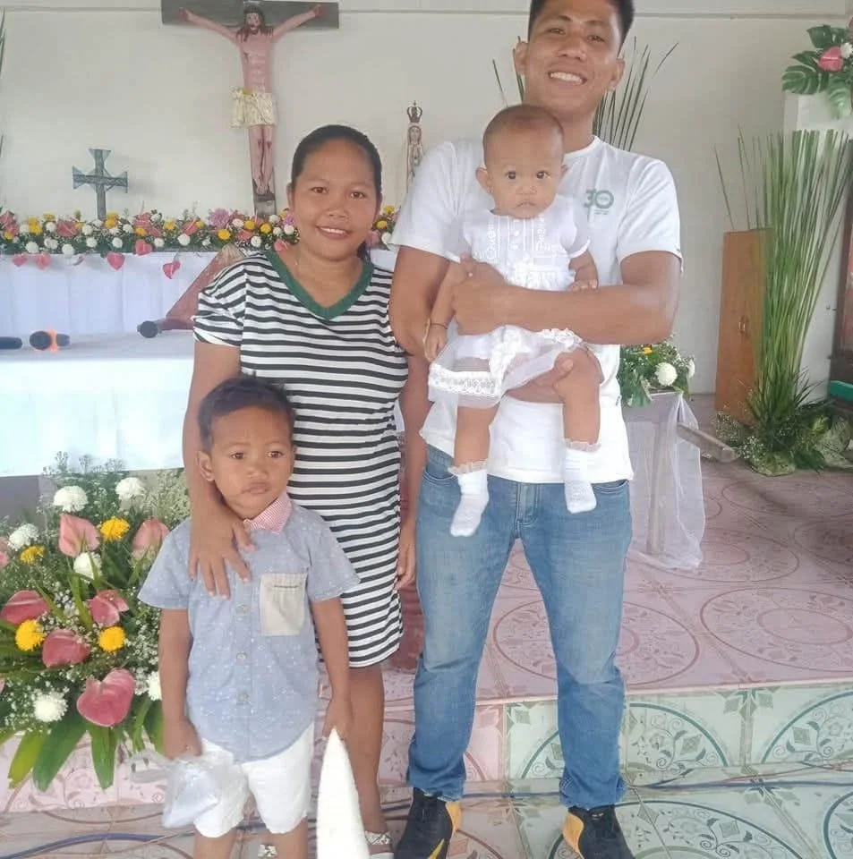 A family of four, including a man, woman, and two children, standing inside a church with religious images and floral decorations, during a special occasion.