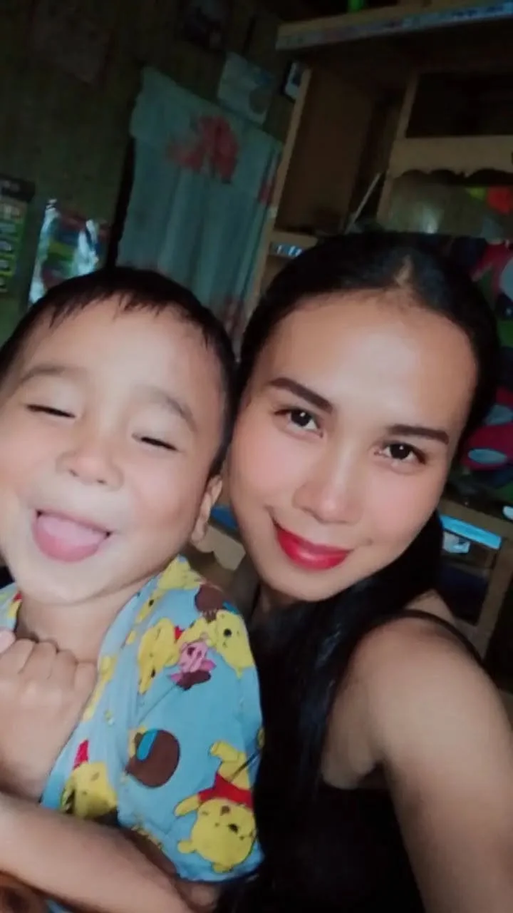 A woman and a young boy smiling and taking a selfie together indoors.