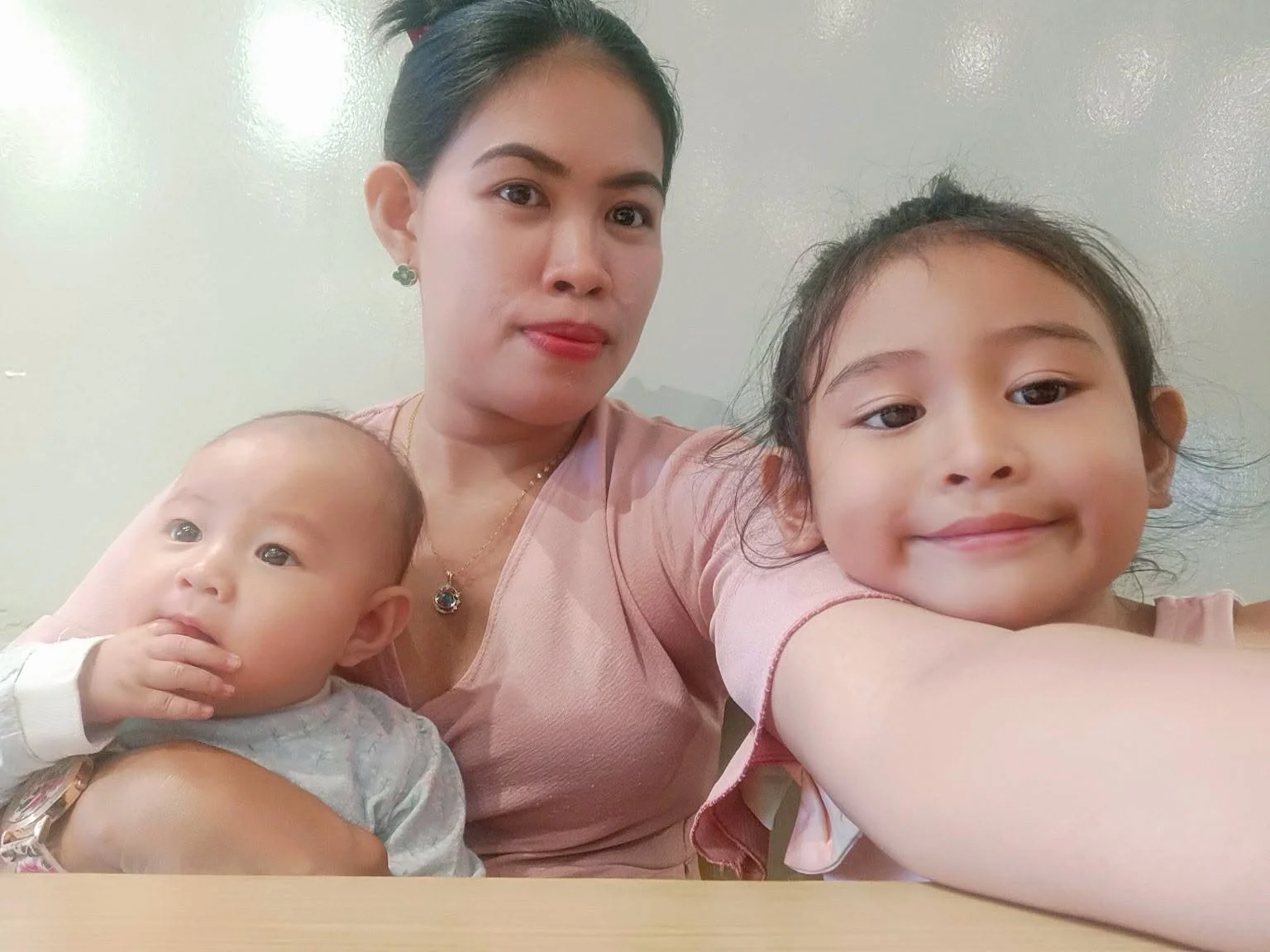 A woman taking a selfie with two children, one baby and a young girl, sitting close together.