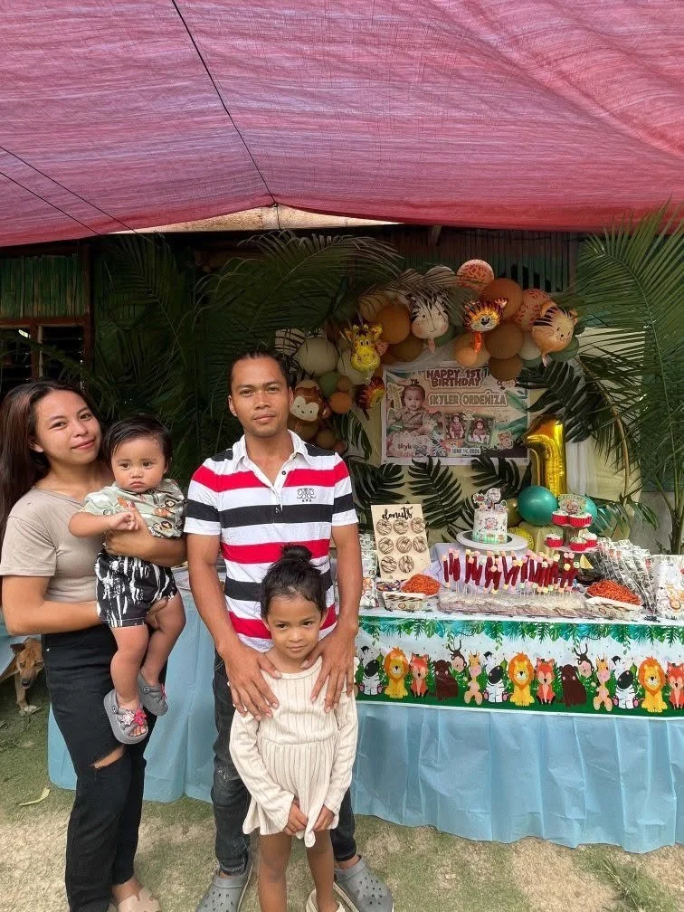 Family celebrating a child's birthday with a decorated table, balloons, and jungle-themed decorations outdoors.