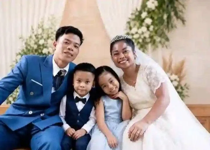 Family of five dressed in formal wedding attire sitting together and smiling indoors.