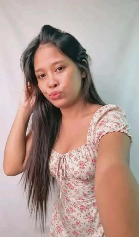 A woman with long, dark hair taking a selfie against a plain wall, wearing a floral-patterned top with puffed sleeves.