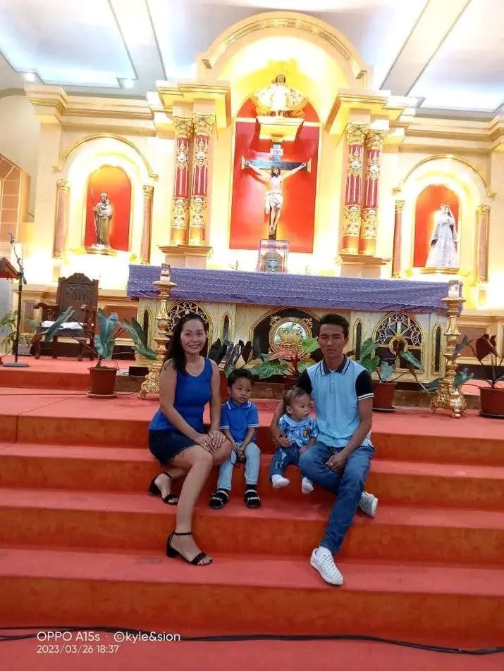 A family of four sitting on the steps inside a church, with religious statues and a crucifix in the background.