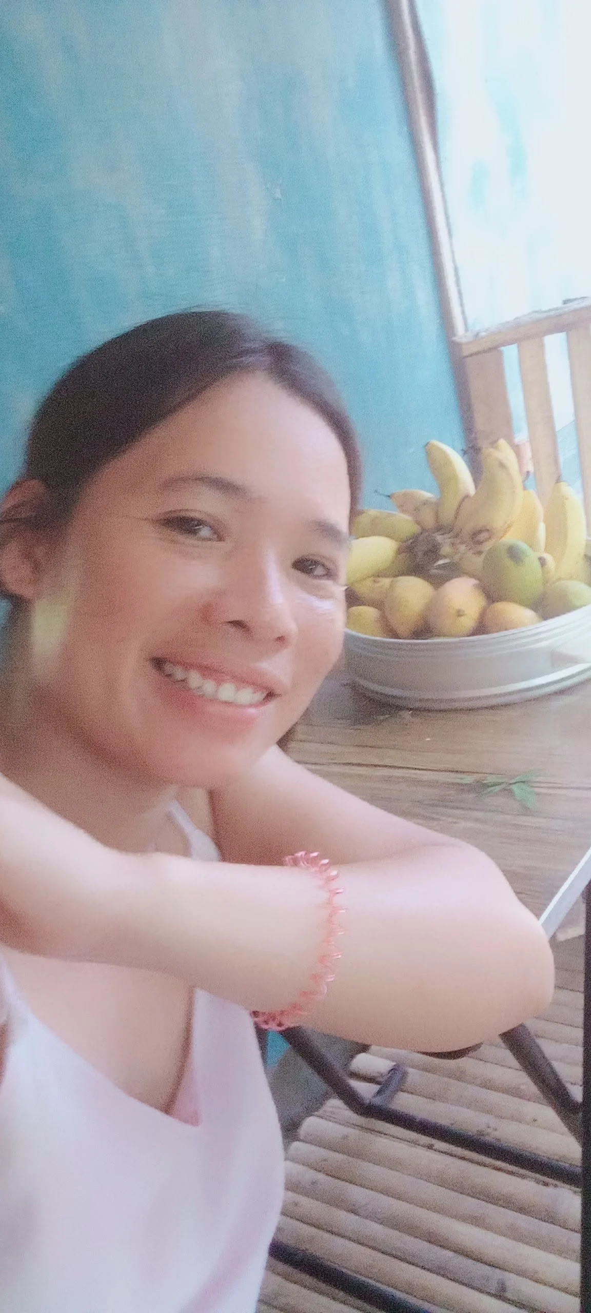 Smiling woman with dark hair taking a selfie, with a bowl of bananas and other fruit in the background.
