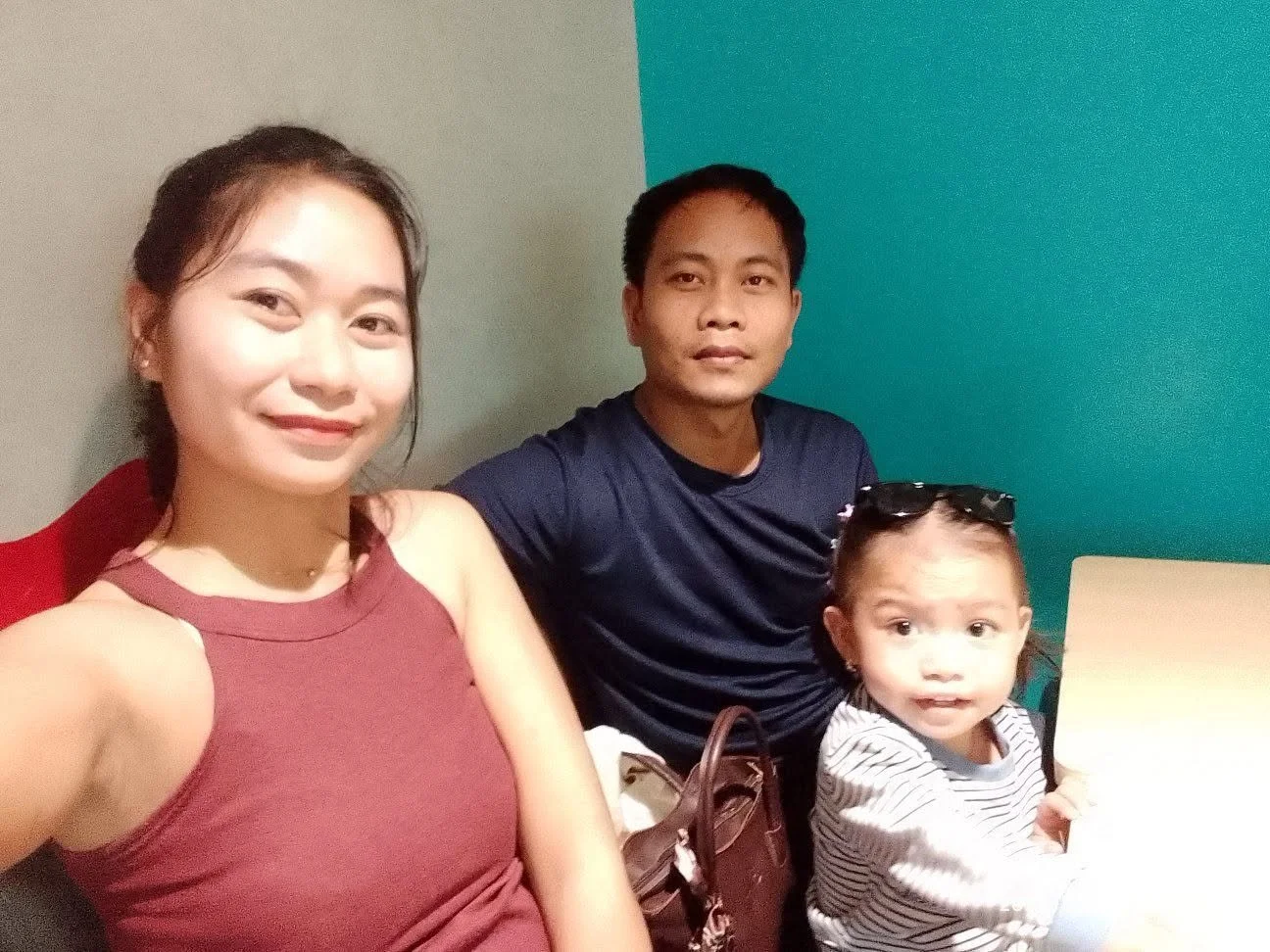 A smiling woman, a man, and a young girl sitting together in a room with green and gray walls.