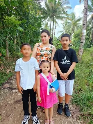 Four children standing on a dirt path in a tropical setting with palm trees and lush greenery.