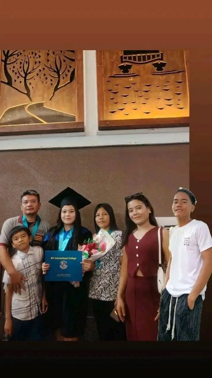 Woman in graduation cap and gown holding a diploma and bouquet, surrounded by family members at graduation ceremony.