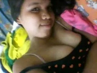 A woman with short dark hair lying down with colorful clothing around her, wearing a black top with pink heart patterns.