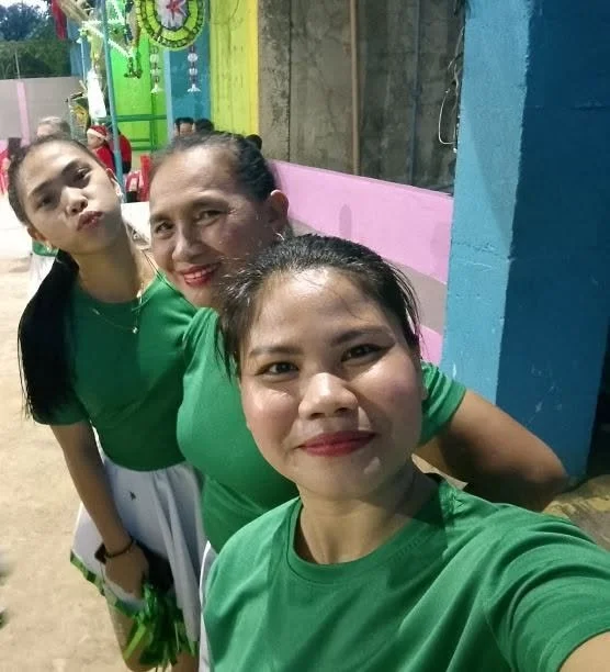 Three women and a girl taking a selfie outdoors near a colorful building, all wearing green shirts.