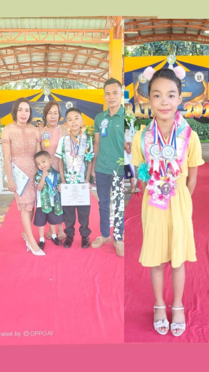 Group of children and adults at an award ceremony, with children wearing medals and holding certificates, standing on a red carpet under a covered outdoor area, with a decorated backdrop in the background.
