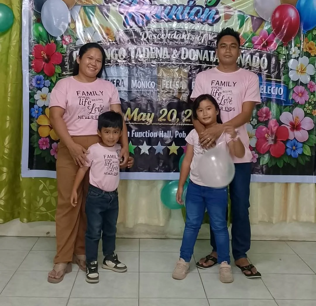 Family group at a celebration with a colorful balloon and floral decorated backdrop. Two women and two children are posing, all smiling.