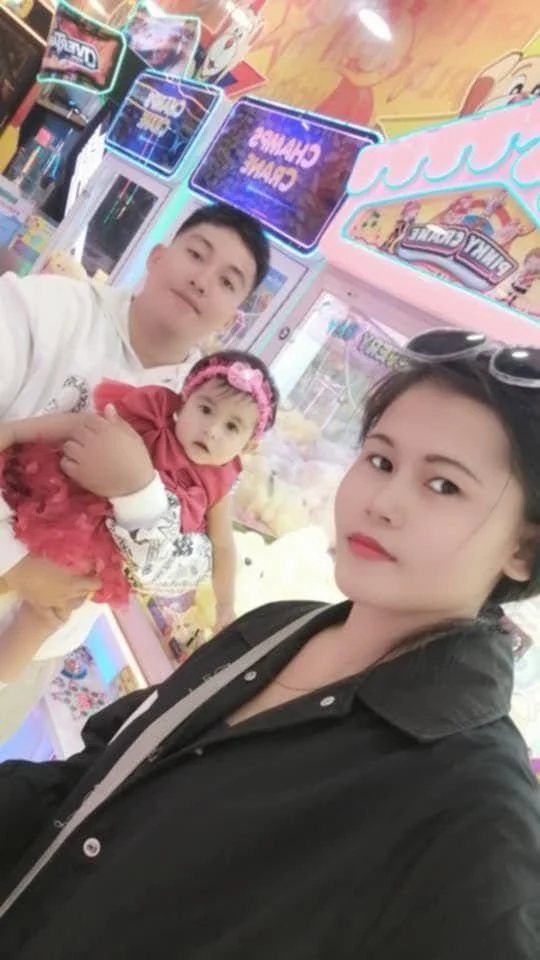 A woman taking a selfie in an arcade with a man and a young girl, with colorful arcade games and claw machines in the background.
