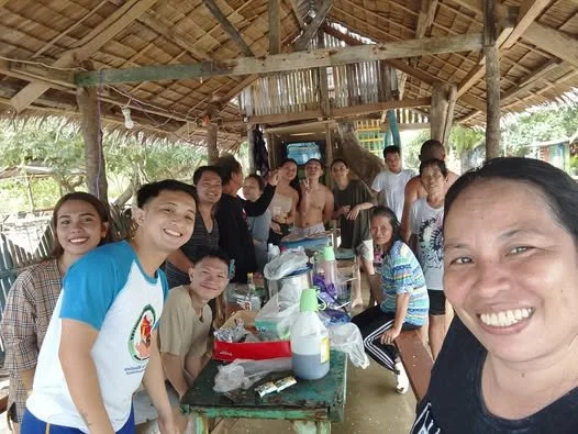 Group of people smiling and gathered around a table in a rustic outdoor setting.
