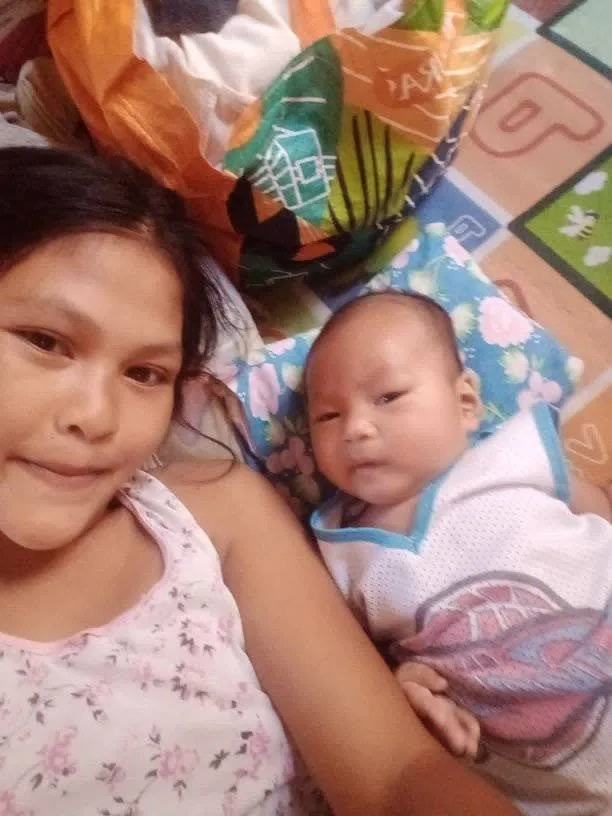 A woman lying down next to a baby on a colorful blanket with a bag of chips or snacks behind them.