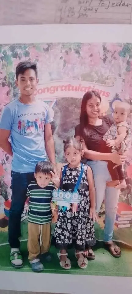Family photo of four children and a woman, with a 'Congratulations' banner in the background, taken at an indoor celebration.