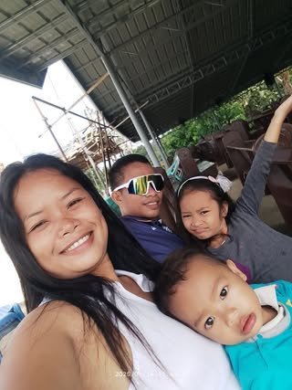 A group of four people taking a selfie outdoors, with a woman, two children, and a young man wearing sunglasses, all smiling and posing happily.