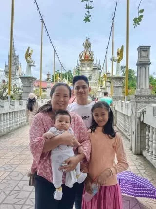 Family of four standing together at a temple with decorative minarets and a white balustrade, cloudy sky in the background.