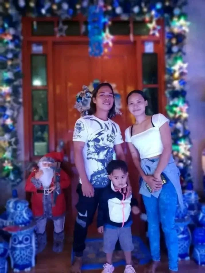 Two young girls and a young boy posing in front of a Christmas-themed decoration with a Santa Claus figure in the background.