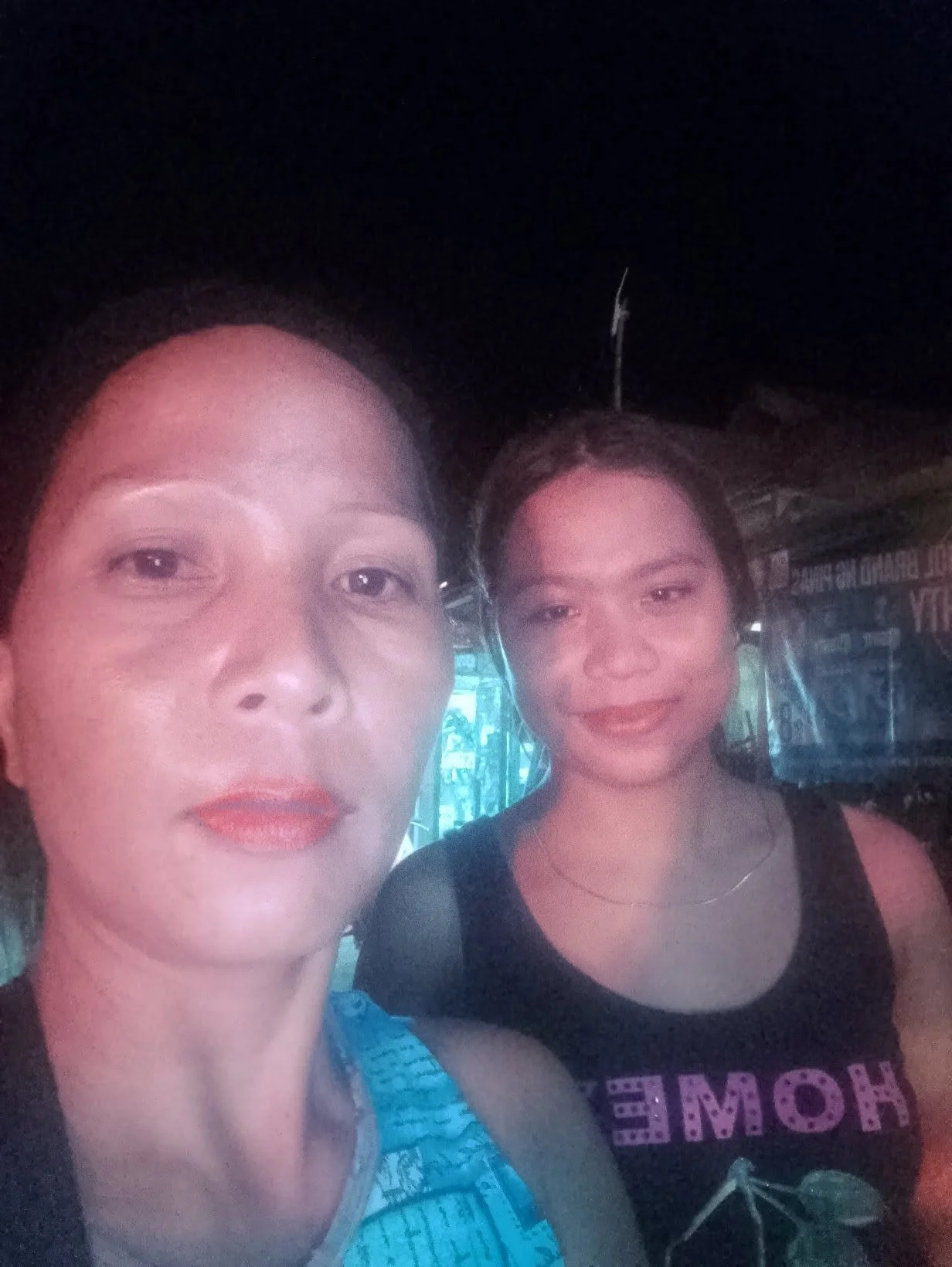 Two women taking a selfie together indoors at night, both smiling and wearing dark clothing.